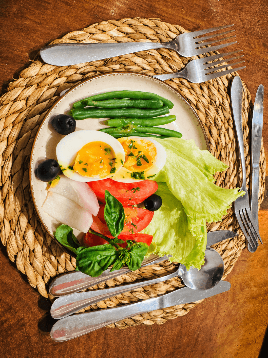 Overhead breakfast plate at The Elephant Oasis — halved boiled eggs, green beans, tomatoes, olives, and basil on a woven placemat, Murchison Falls Uganda