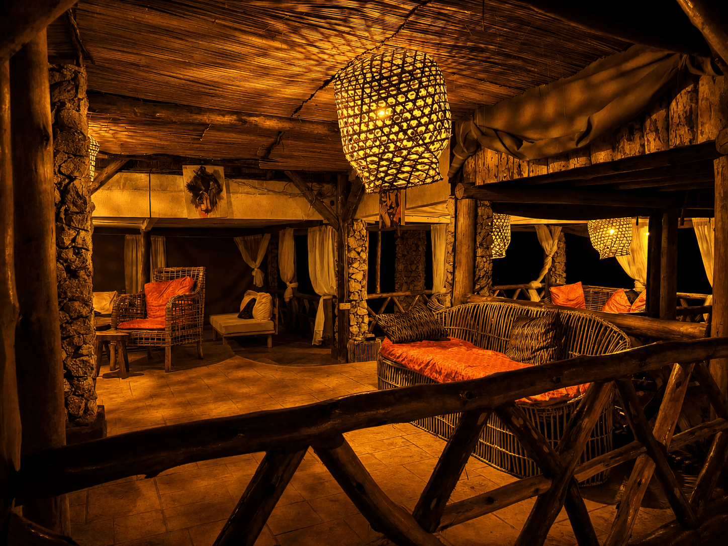 The Elephant Oasis lounge interior at night — woven pendant lantern, stone walls, timber poles, rattan furniture with orange cushions, Murchison Falls Uganda